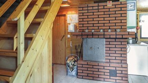 En trätrappa leder upp till en övre våning med en öppen planlösning, en tegelkamin och en klocka på väggen.