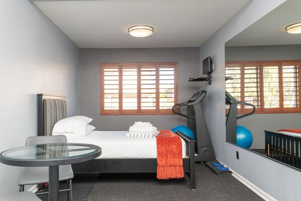 A compact bedroom with a bed, a treadmill, a small exercise ball, and a mirror.