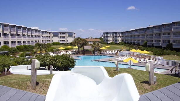 A resort with a pool area, including a water slide, lounge chairs, and umbrellas.