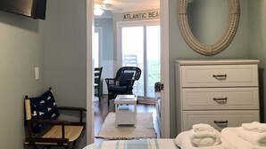 A bedroom with a bed, a dresser, a mirror, and a chair. There is a sign that reads "ATLANTIC BEACH" in the background.