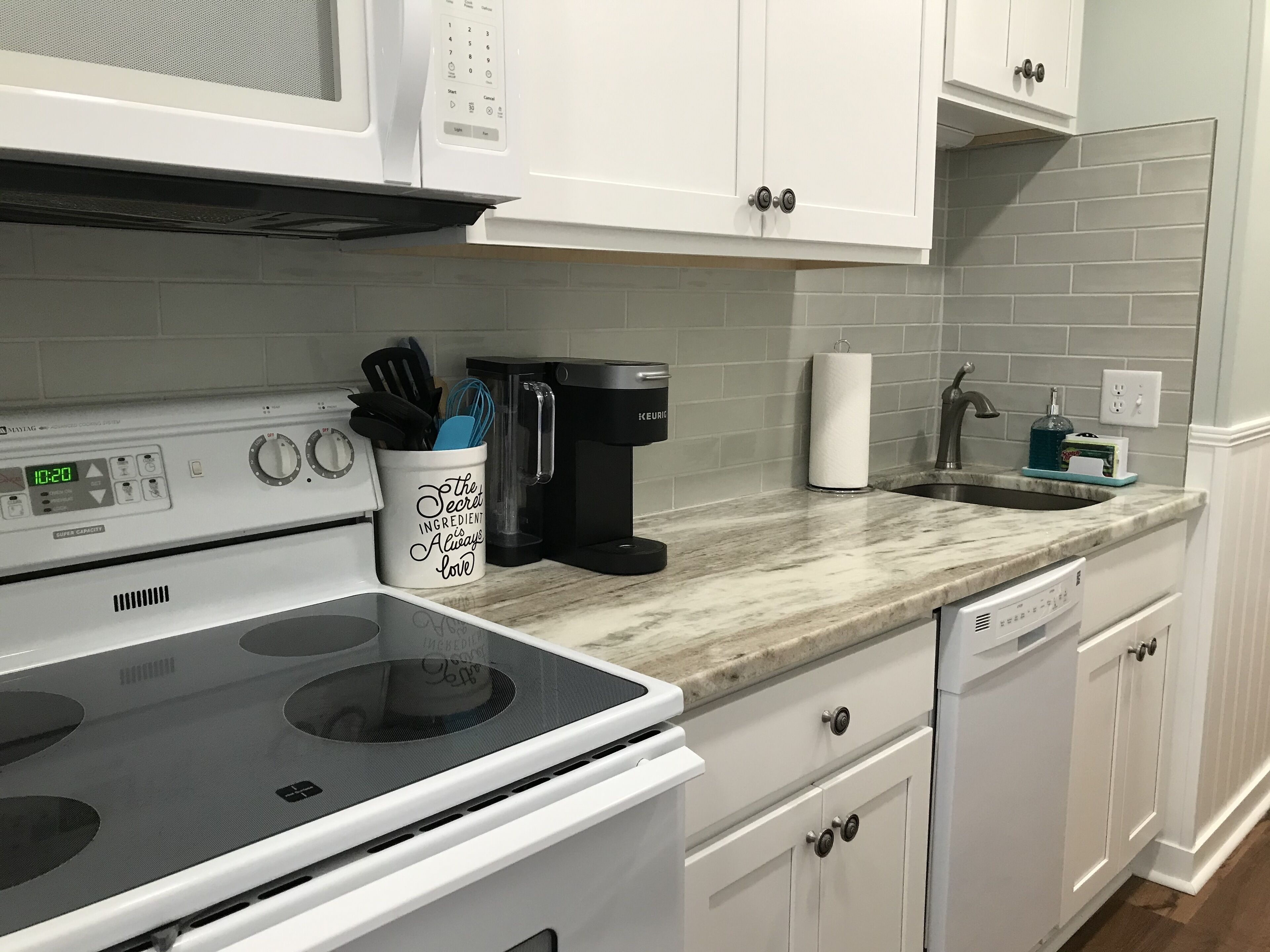 Uma cozinha com armários brancos, uma cafeteira preta, um suporte para papel toalha e uma máquina de lavar louça.