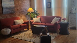 Ein Wohnzimmer mit Backsteinwand, einem roten Sofa, einem Couchtisch, einer Lampe und einer kleinen Hundestatue.