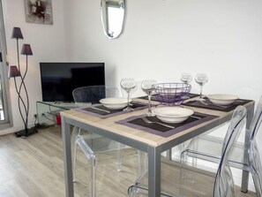 Ein moderner Essbereich mit einem Glastisch, transparenten Stühlen und einem Fernseher im Hintergrund.