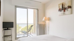 A hotel room with a bed, a TV on a stand, a balcony with a chair, and a painting on the wall. - Apartment Claire by Interhome (Arcachon)