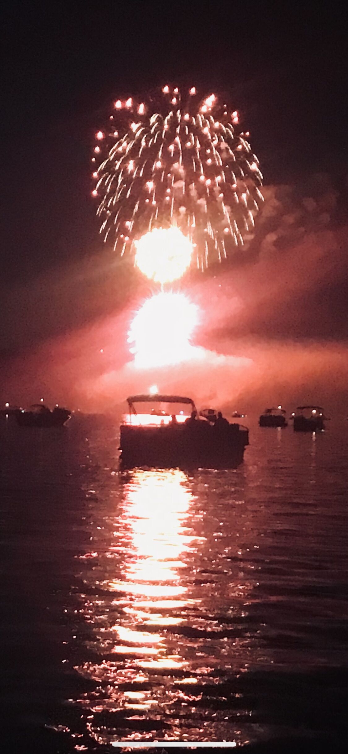 Un bateau sur une eau calme, avec une lumière vive qui scintille au loin, peut-être un feu d'artifice.