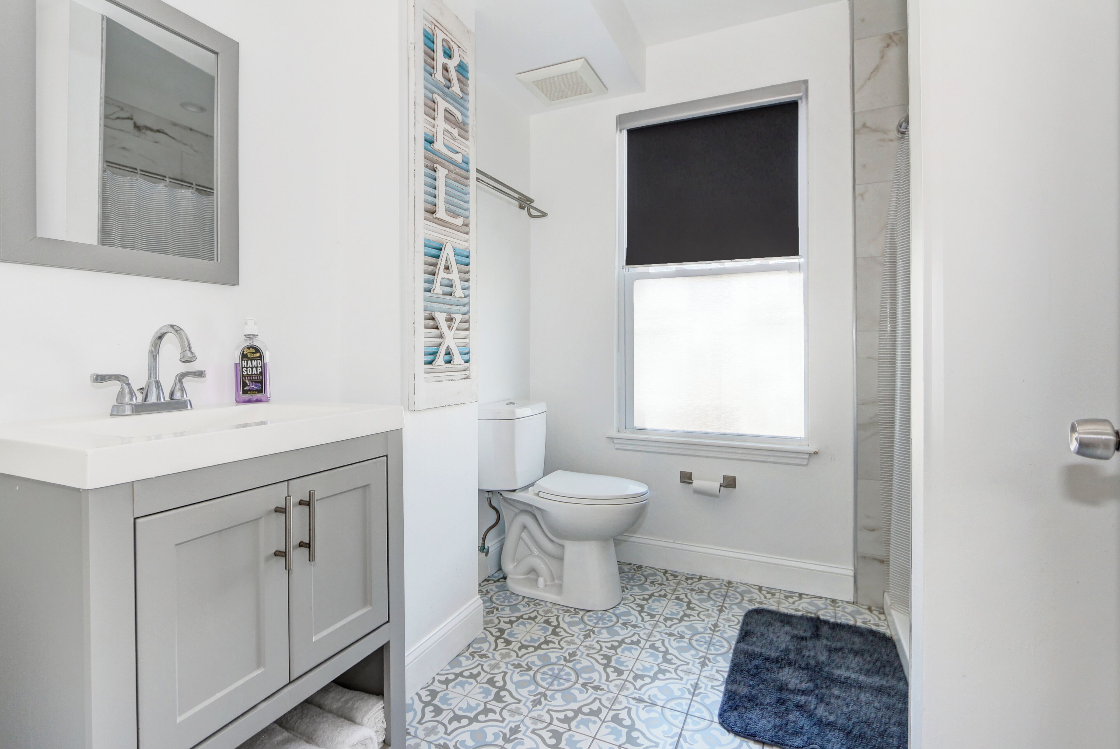 Un baño con lavamanos blanco, inodoro, ducha y baldosas de suelo estampadas.