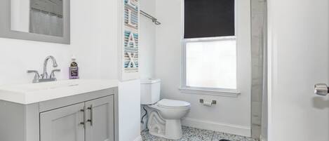 Un baño con lavamanos blanco, inodoro, ducha y baldosas de suelo estampadas.