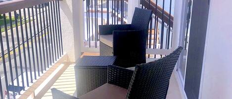 Un balcón con mobiliario de mimbre, barandilla y vista a la calle y edificios.