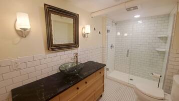 A bathroom with a glass bowl sink, wooden vanity, white subway tiles, a glass shower enclosure, and a toilet.