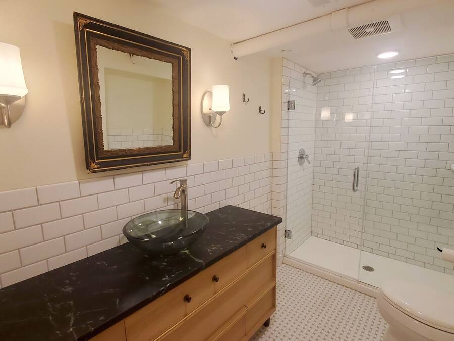 A bathroom with a glass bowl sink, wooden vanity, white subway tiles, a glass shower enclosure, and a toilet.