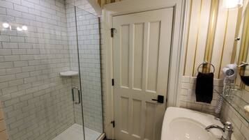 Un baño con cabina de ducha de vidrio, un lavabo blanco y una puerta con una toalla colgada en el pomo.