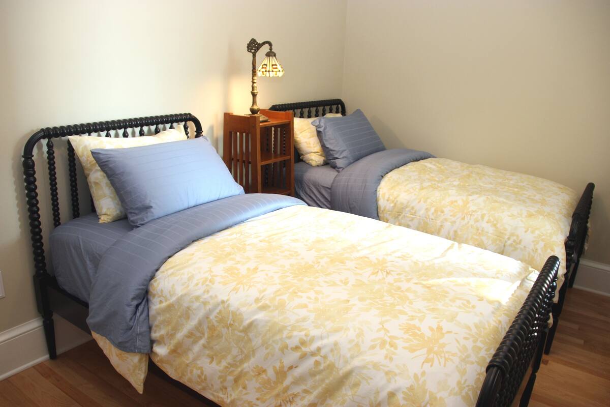 A bedroom with two single beds, a nightstand with a lamp, and a wooden floor.