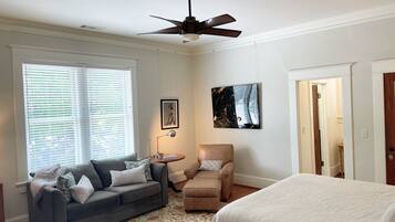 A bedroom with a bed, a gray sofa, a brown armchair, a ceiling fan, and a painting on the wall.