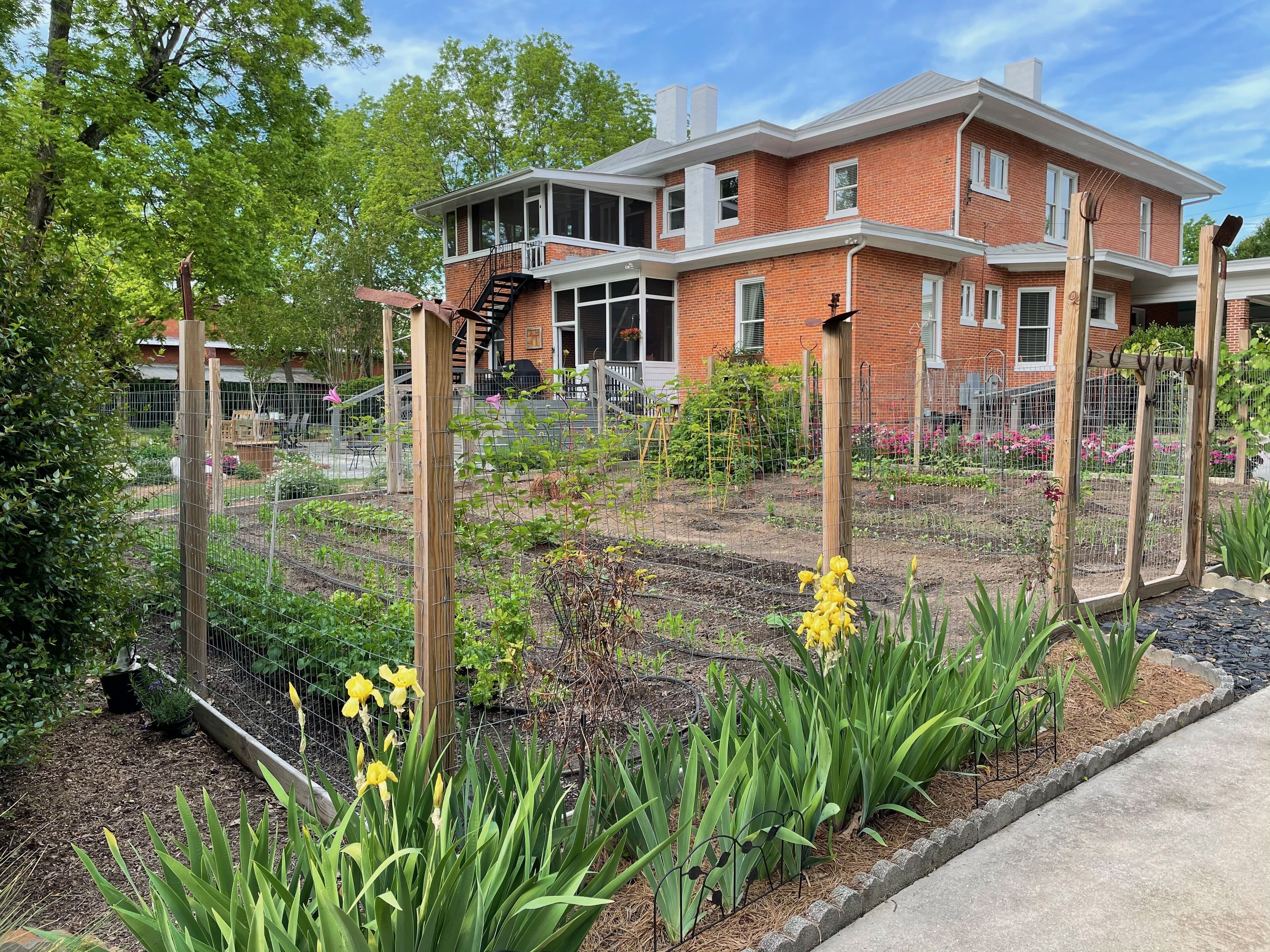 A two-story brick building with a balcony and a garden area with plants and flowers.