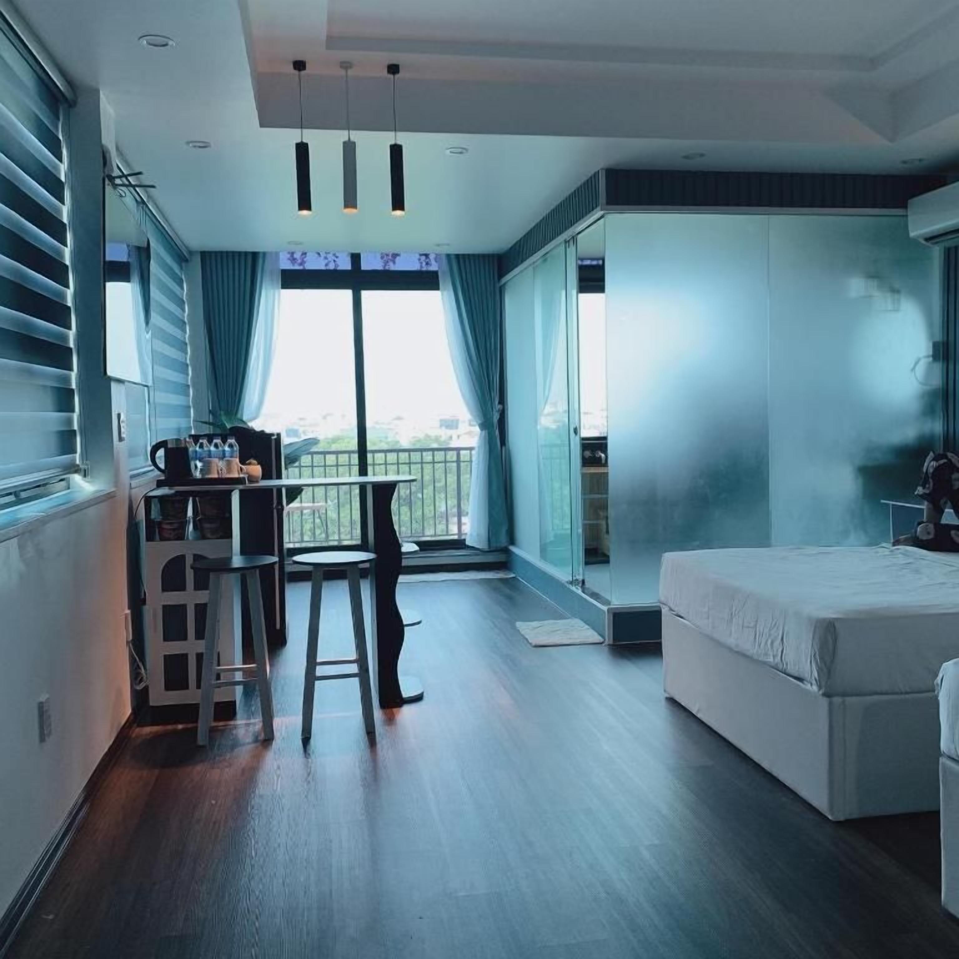 Habitación de hotel moderna con balcón, una cama, un escritorio con silla y una pequeña zona de kitchenette.