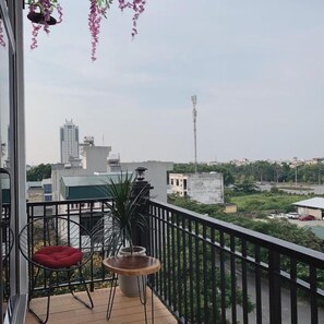 A balcony with a chair, a small table, and hanging plants. - Mio Hotel (Hai Phong)