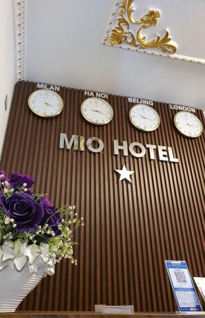 A hotel reception desk with clocks displaying times for Milan, Hanoi, Beijing, and London. - Mio Hotel (Hai Phong)