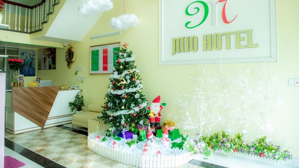 Zona de recepción de un hotel con un árbol de Navidad, un letrero que dice "JUNIO HOTEL" y una escalera de fondo.