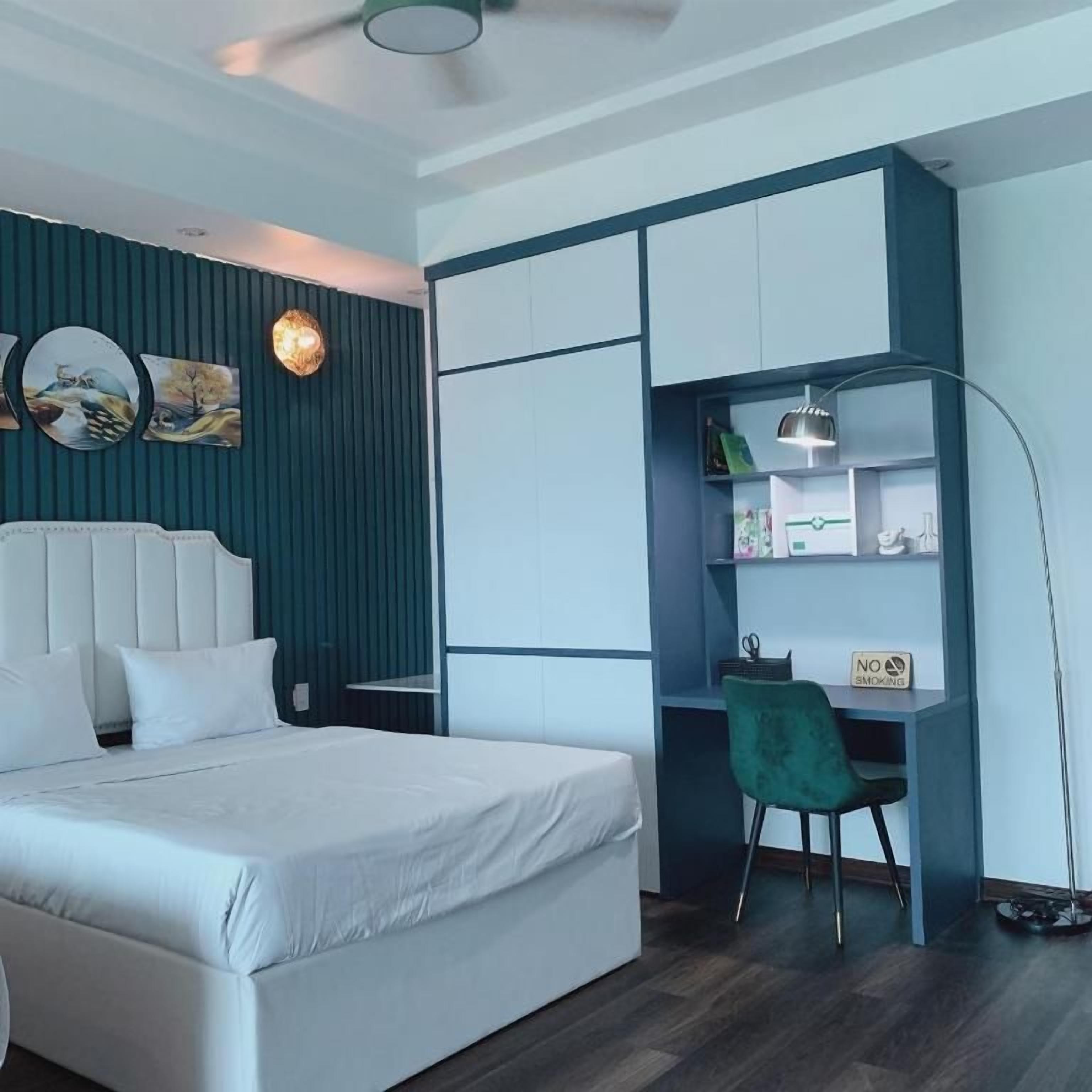 A modern bedroom with a bed, a desk, and a chair. There is a 'NO SMOKING' sign on the desk.