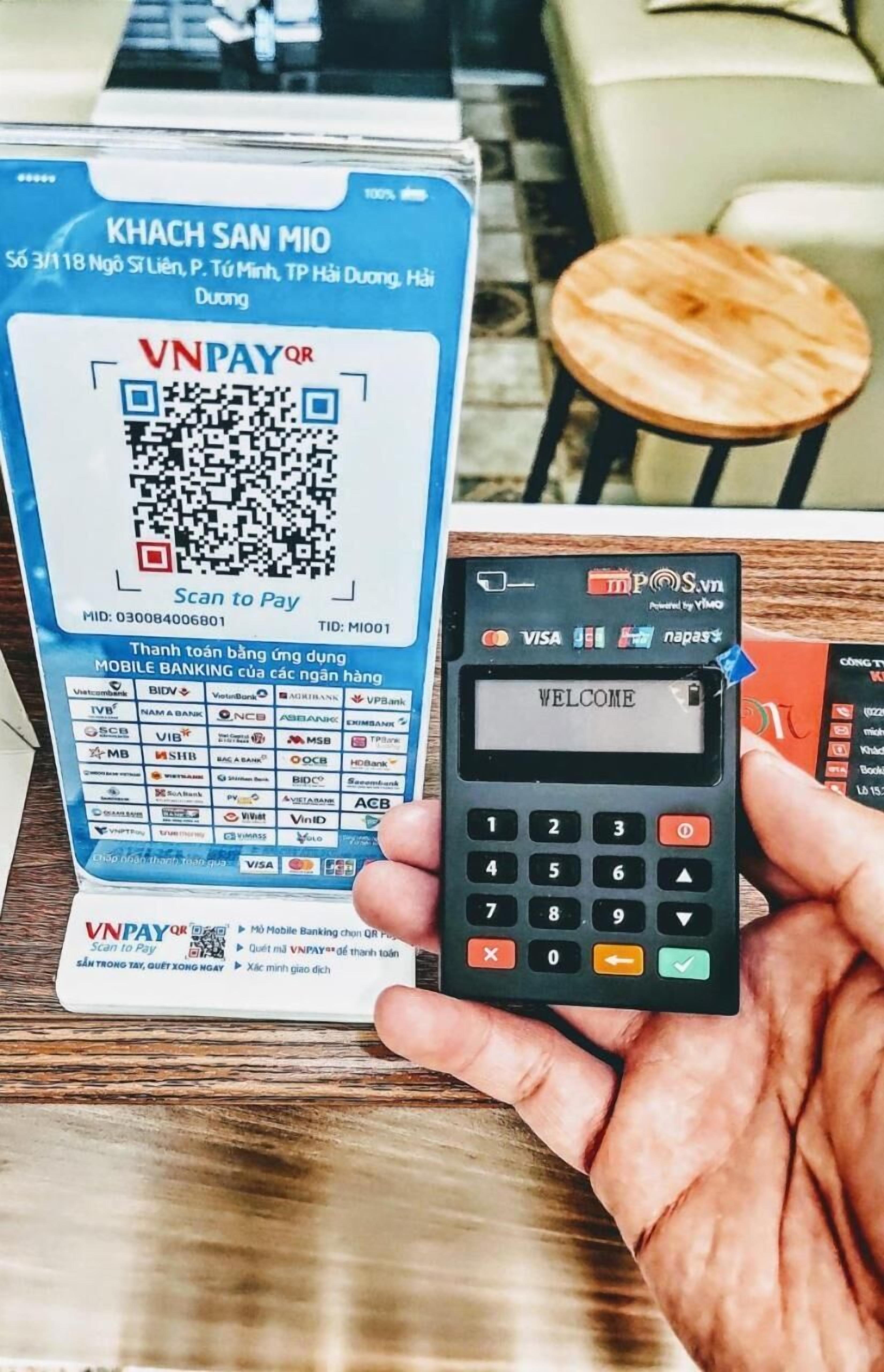 Uma mão segurando um dispositivo de pagamento móvel com um código QR e um cartão.