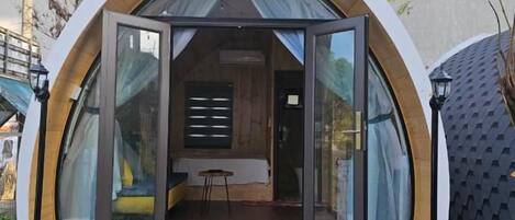 A modern, semi-open structure with a bench and potted plants in front, and a small table inside.