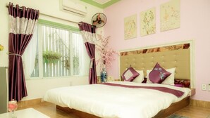 Un dormitorio con una cama grande, una mesita de noche, una ventana con cortinas, un ventilador y una obra de arte en la pared.