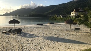 En strand med stråtagsparasoller, liggestole og et hus med rødt tag.