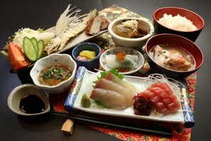 Verschiedene japanische Gerichte, darunter Sashimi, Reis und Suppe, präsentiert auf einem Tisch mit Stäbchen und kleinen Schalen.