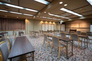 Una sala de conferències amb diverses taules i cadires, una pantalla gran i una catifa amb dibuixos.