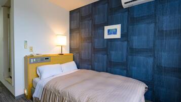 A hotel room with a bed, bedside table, lamp, air conditioning unit, and a wall with a blue abstract pattern.