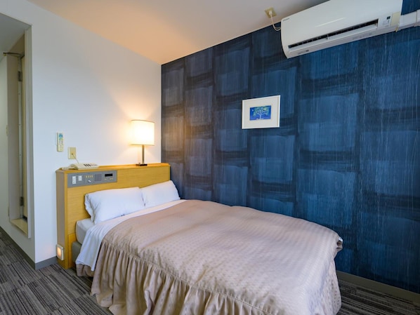 A hotel room with a bed, bedside table, lamp, air conditioning unit, and a wall with a blue abstract pattern.