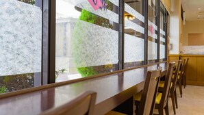 A restaurant with a long counter, chairs, and a view through frosted glass windows. - Hisai Green Hotel (Tsu)