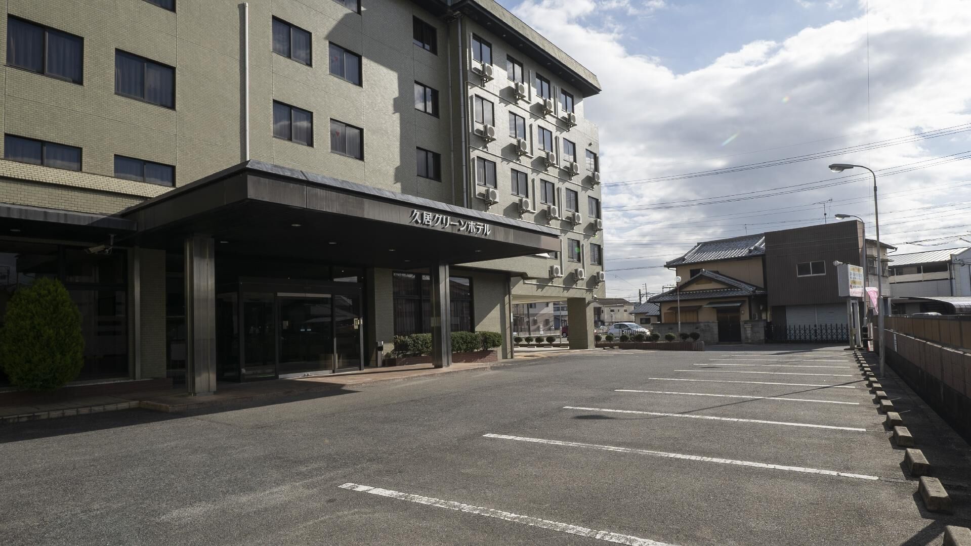 A multi-story hotel with a covered entrance, a parking lot, and a traditional building in the background.
