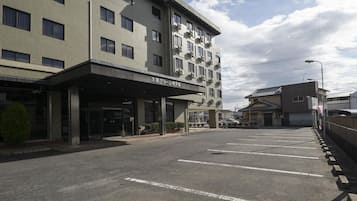 A multi-story hotel with a covered entrance, a parking lot, and a traditional building in the background.