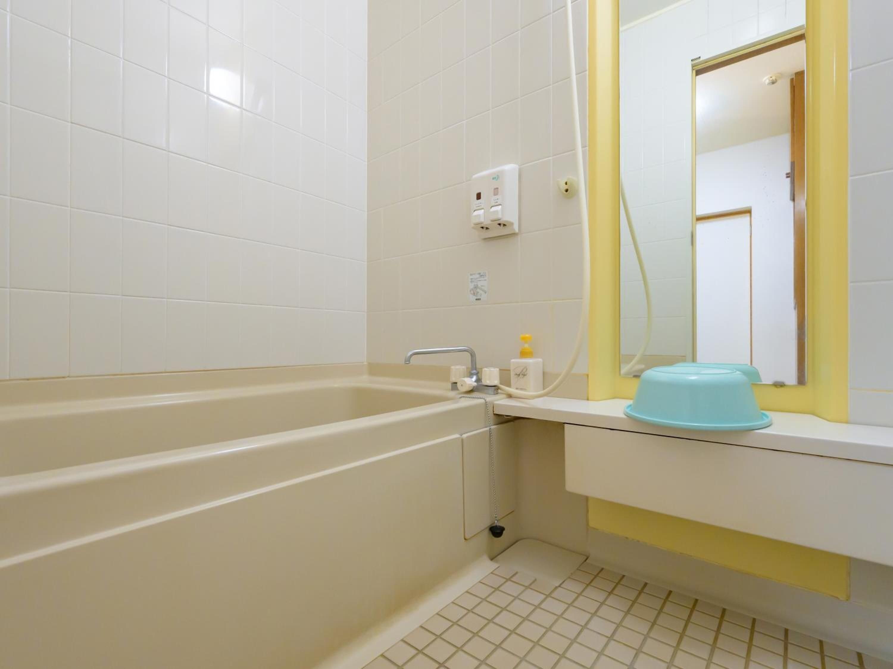 Une salle de bain avec une baignoire, un lavabo, un miroir et un porte-serviettes jaune.