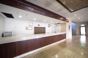 A hotel reception area with a wooden counter, a clock, and a framed certificate on the wall.