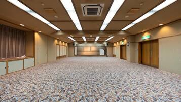 A large, empty hotel room with a patterned carpet, wooden paneling, and a long corridor leading to a reception area.
