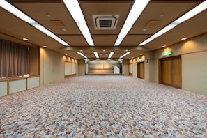 A large, empty hotel room with a patterned carpet, wooden paneling, and a long corridor leading to a reception area.