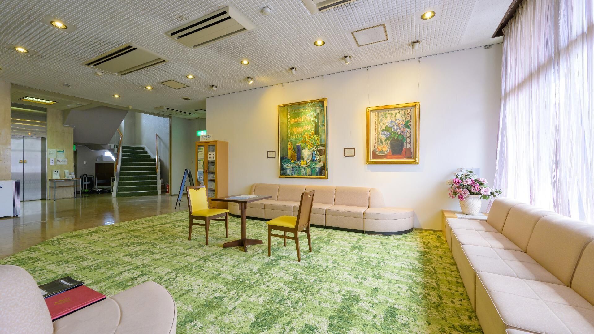 En hotellobby med ett grönt, mönstrat golv, en soffa, stolar, ett bord och två tavlor på väggen.