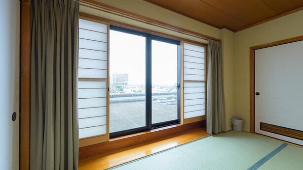 A room with tatami flooring, a sliding shoji door, and a view of a parking lot through large windows. - Hisai Green Hotel (Tsu)