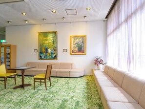 Rebedor d'hotel amb un mosaic verd i motius, un sofà beix, una cadira de fusta, una taula petita i dos quadres emmarcats a la paret.