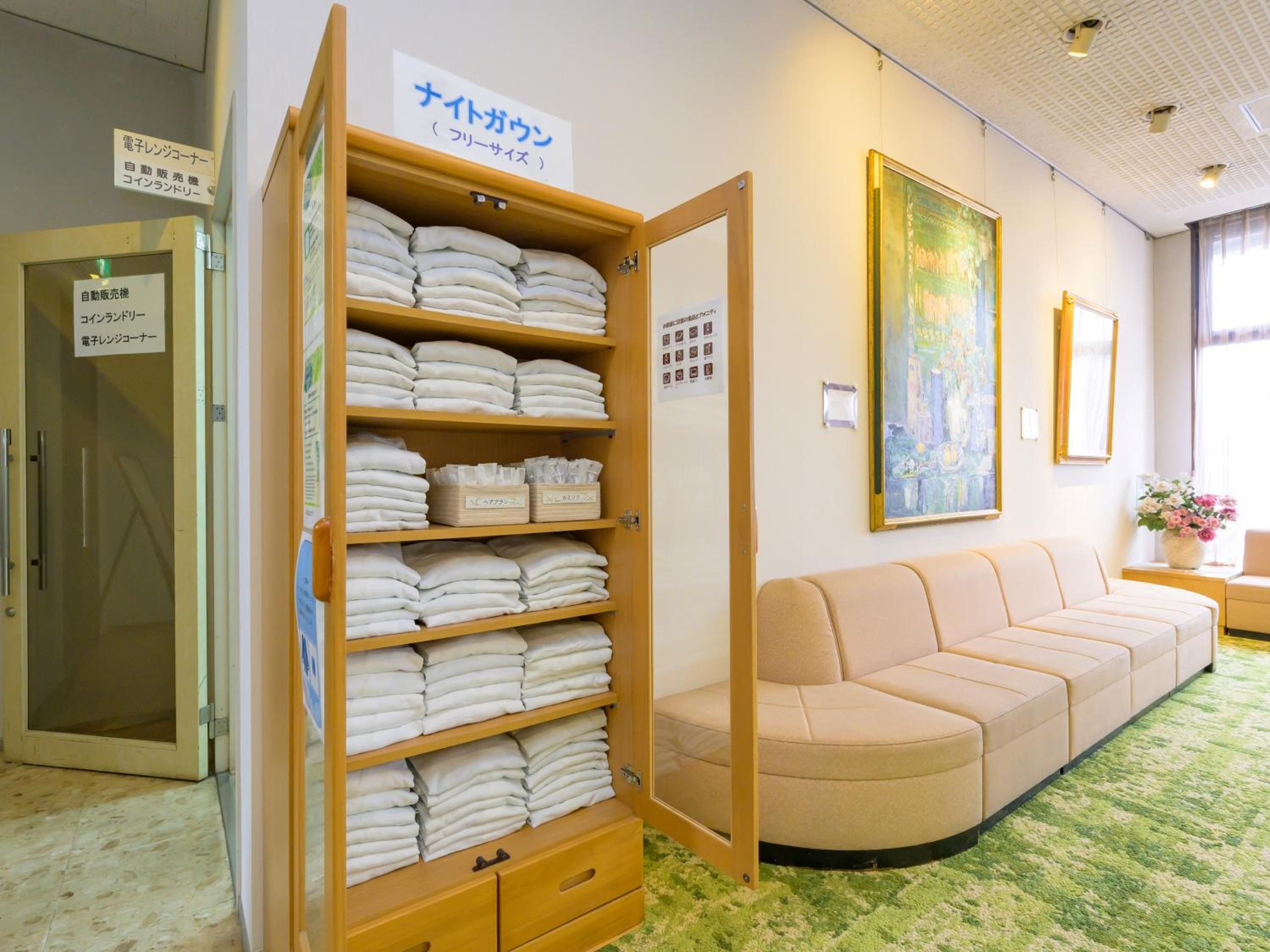 A hotel room with a wooden shelf filled with folded towels, a beige sofa, and a painting on the wall.