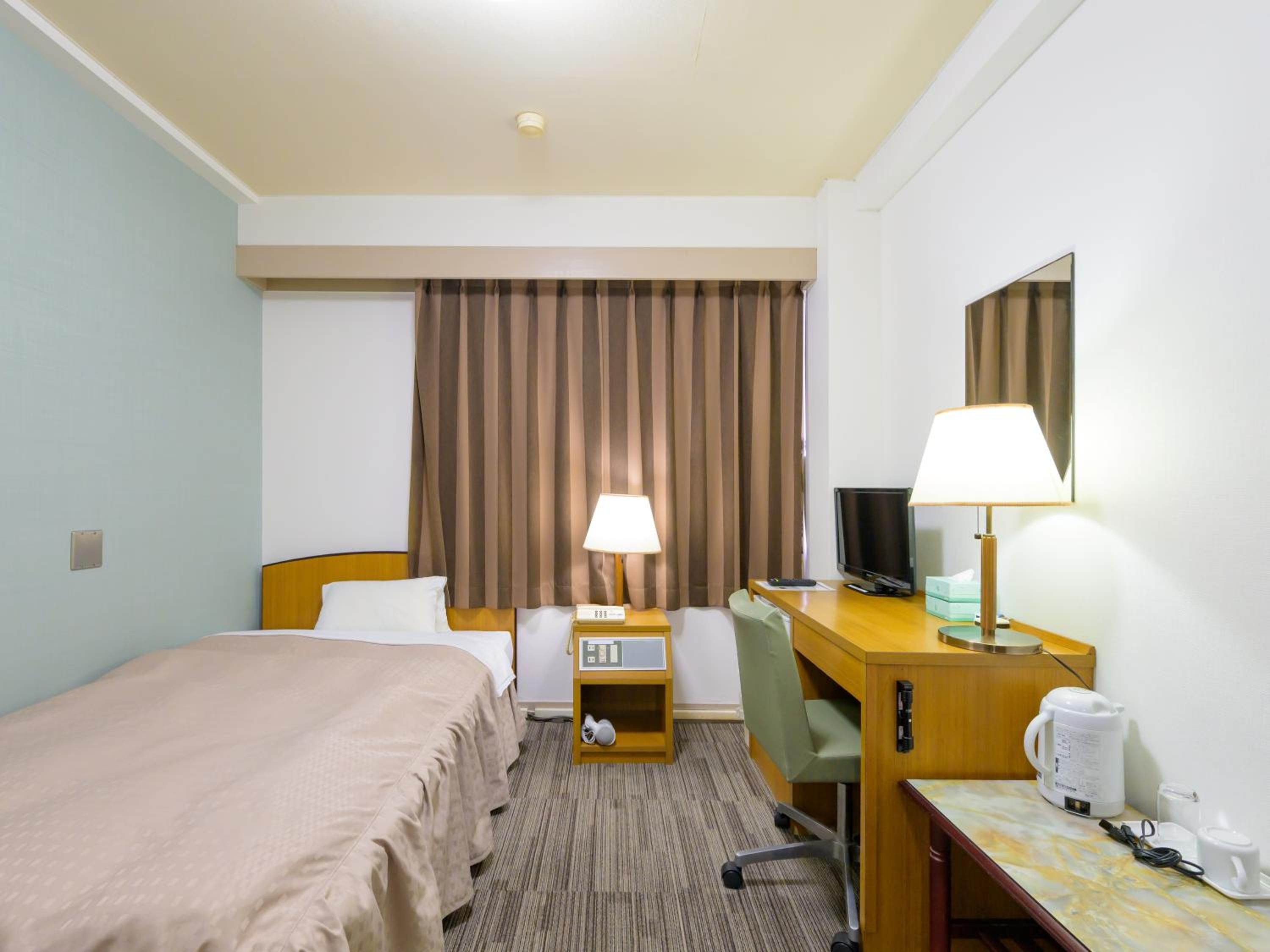 A hotel room with a bed, desk, chair, television, lamps, and a coffee maker.