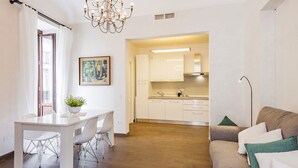 Eine moderne Küche mit weißen Schränken, ein Essbereich mit einem weißen Tisch und Stühlen sowie ein Sofa mit grünen Kissen.