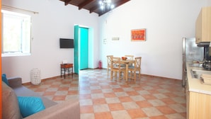A spacious living area with a checkered floor, a dining table with chairs, a sofa, a television, and a kitchen area with a refrigerator.
