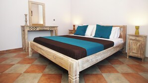 A wooden bed with a brown and teal bedspread, a wooden nightstand with a lamp, and a mirror on a dresser.
