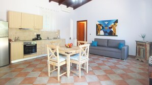 A kitchen with wooden cabinets, a dining table with chairs, a gray sofa, and a painting on the wall.