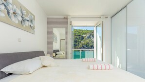 Une chambre à coucher avec un lit, des oreillers, un tableau, un miroir et un balcon donnant sur un paysage montagneux.