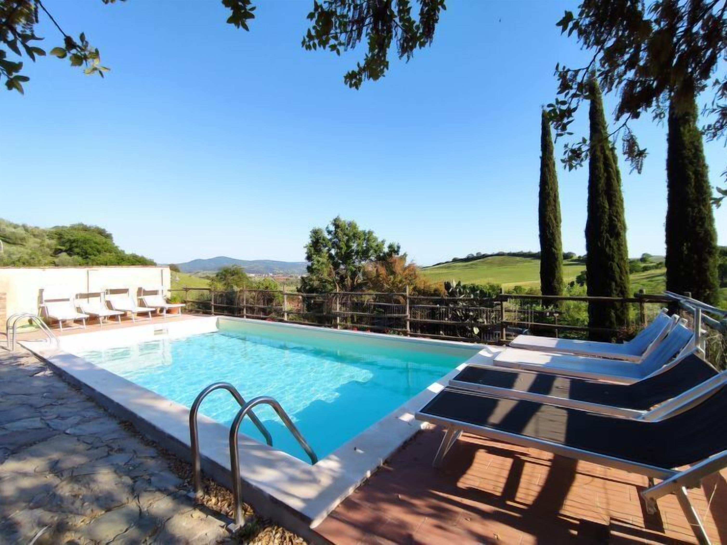 A swimming pool with lounge chairs, a stone deck, and a view of the countryside.