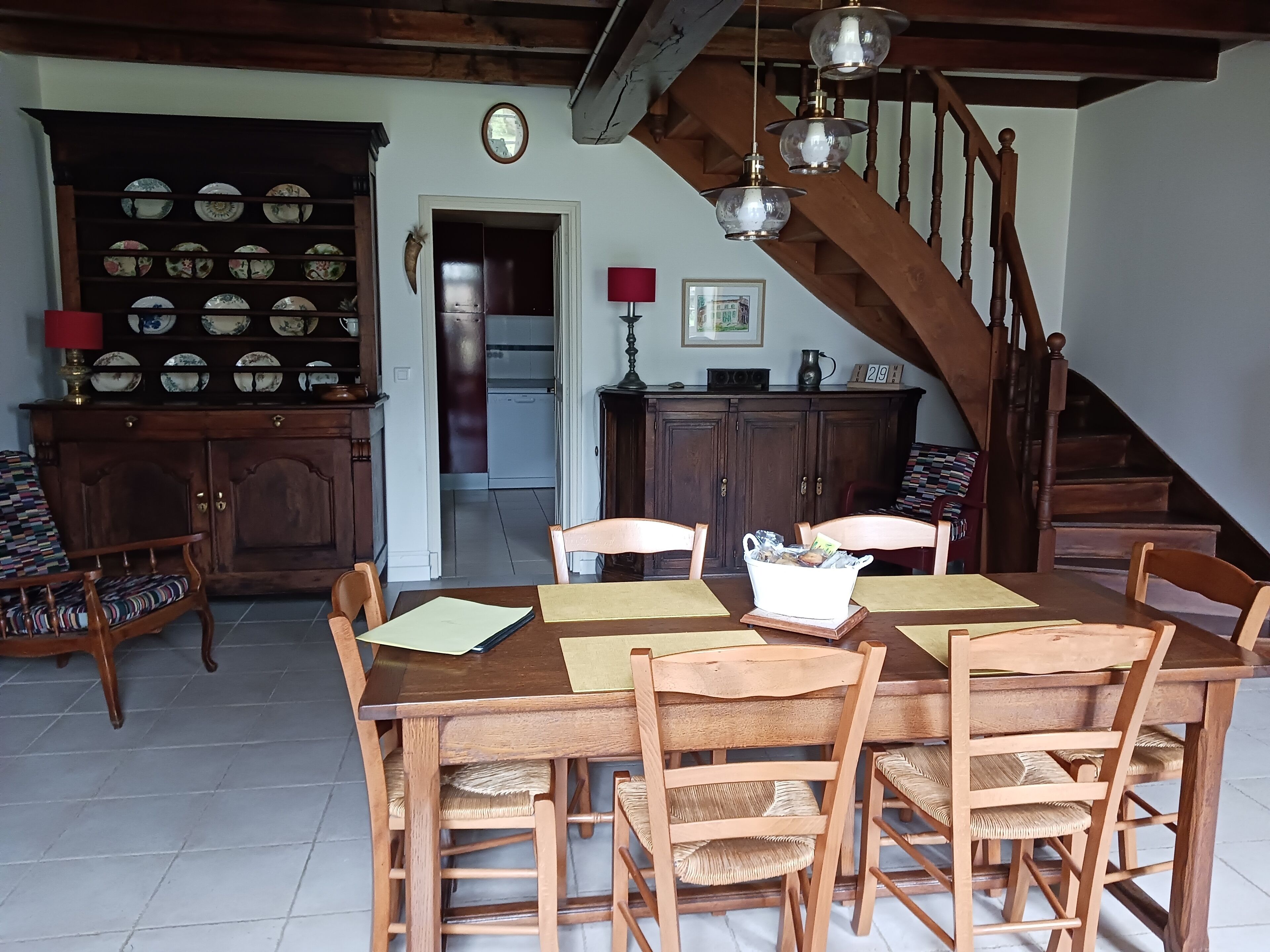 Un coin repas avec une table et des chaises en bois, un buffet contenant de la vaisselle et un escalier.